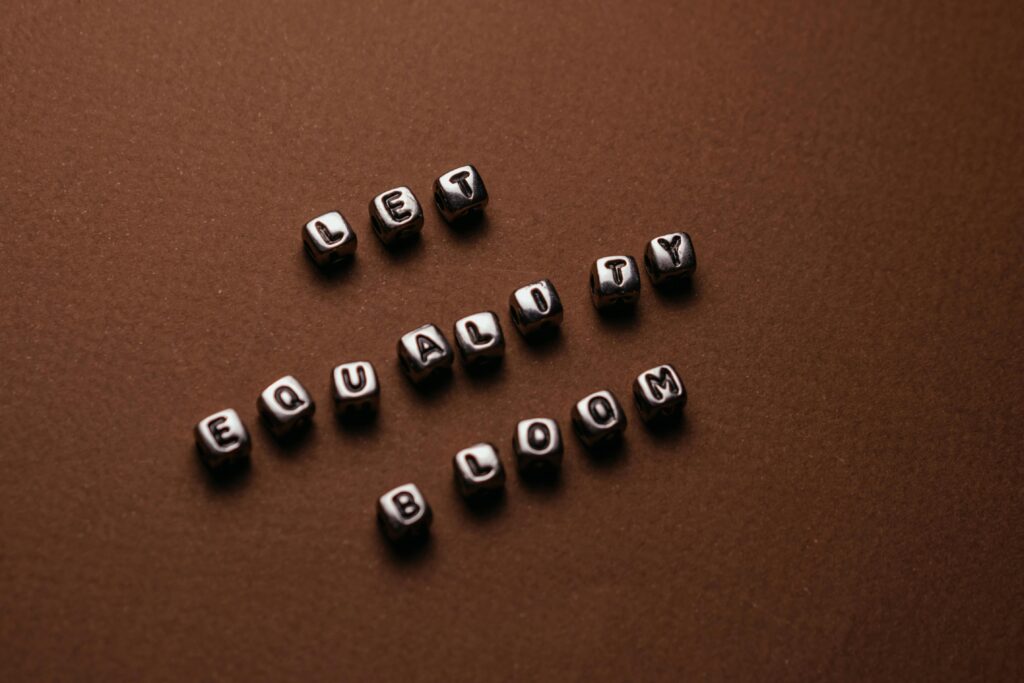 Close-up of 'Let Equality Bloom' spelled with cubes on a brown background, promoting human rights.