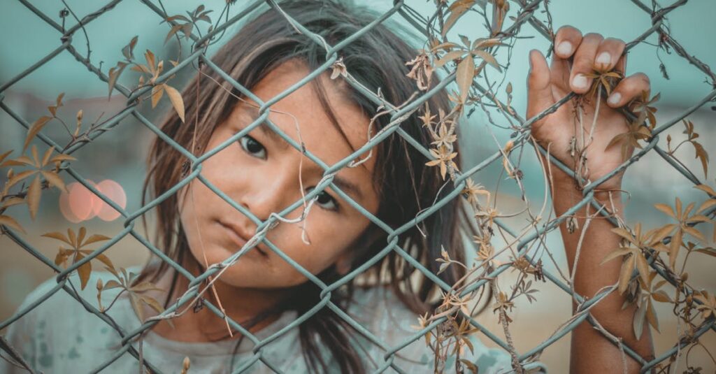 A thoughtful child gazes through a wire fence, symbolizing innocence and curiosity.