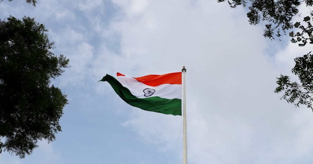 Low angle shot of the Indian national flag on a flagpole with a clear blue sky.