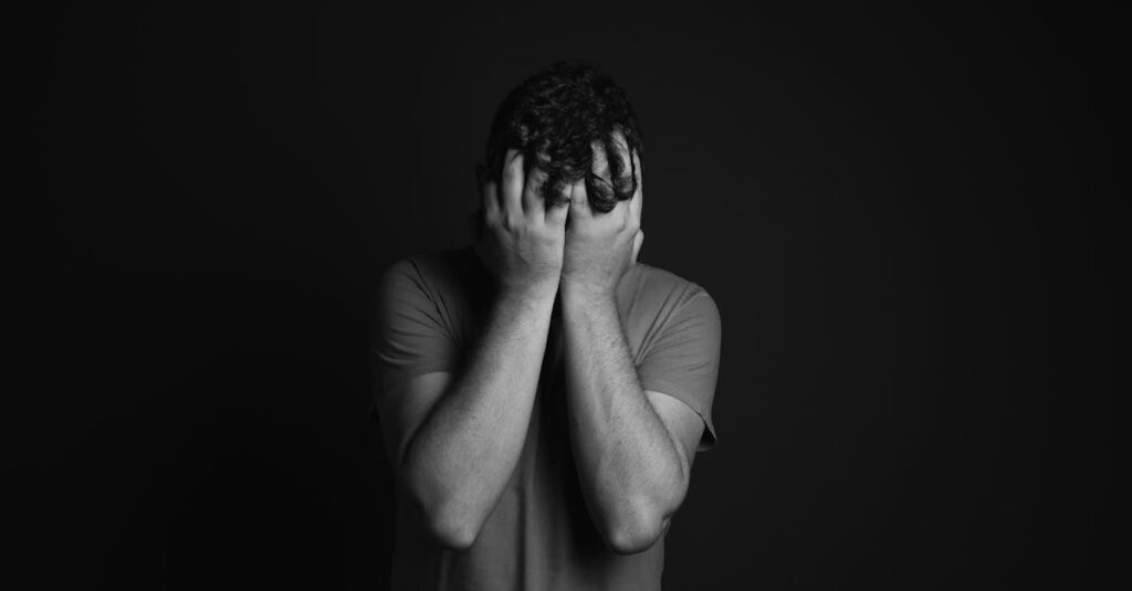 A grayscale portrait of a man covering his face, depicting emotion and mental health themes.