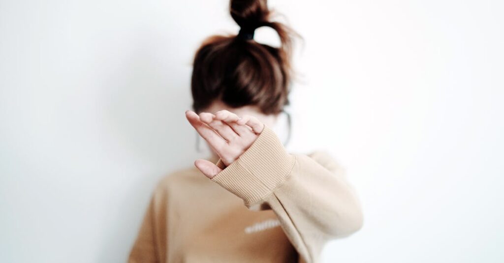 A woman in a sweatshirt raises her hand to cover her face, suggesting stop or privacy.