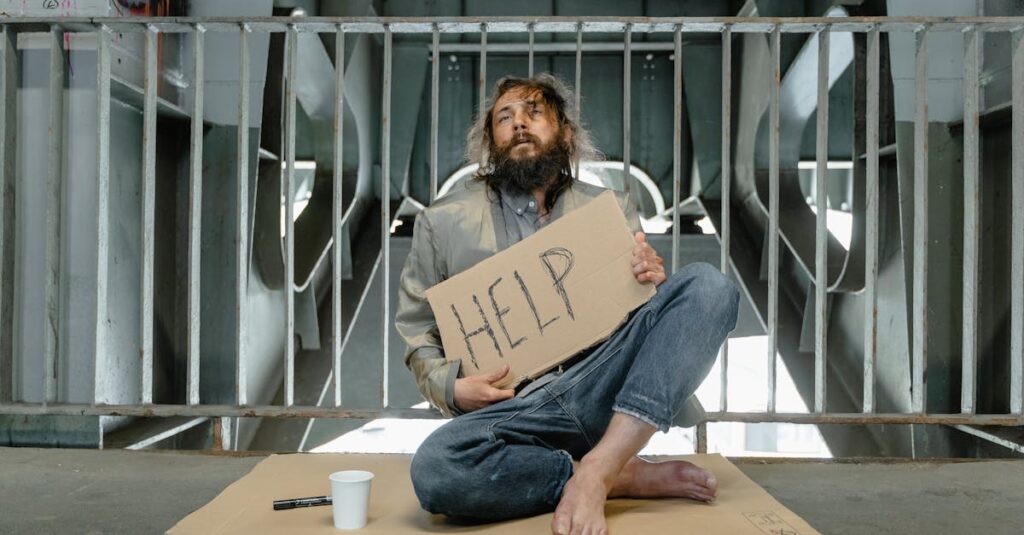 A homeless man sits under a bridge with a sign reading 'HELP', highlighting poverty and homelessness.