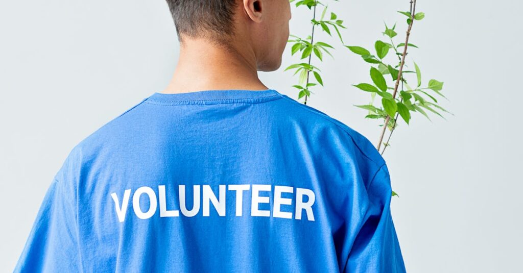 Person in blue volunteer shirt carrying a green plant, viewed from behind.