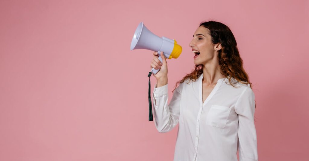 Confident woman using a megaphone against a soft pink background. Perfect for communication concepts.