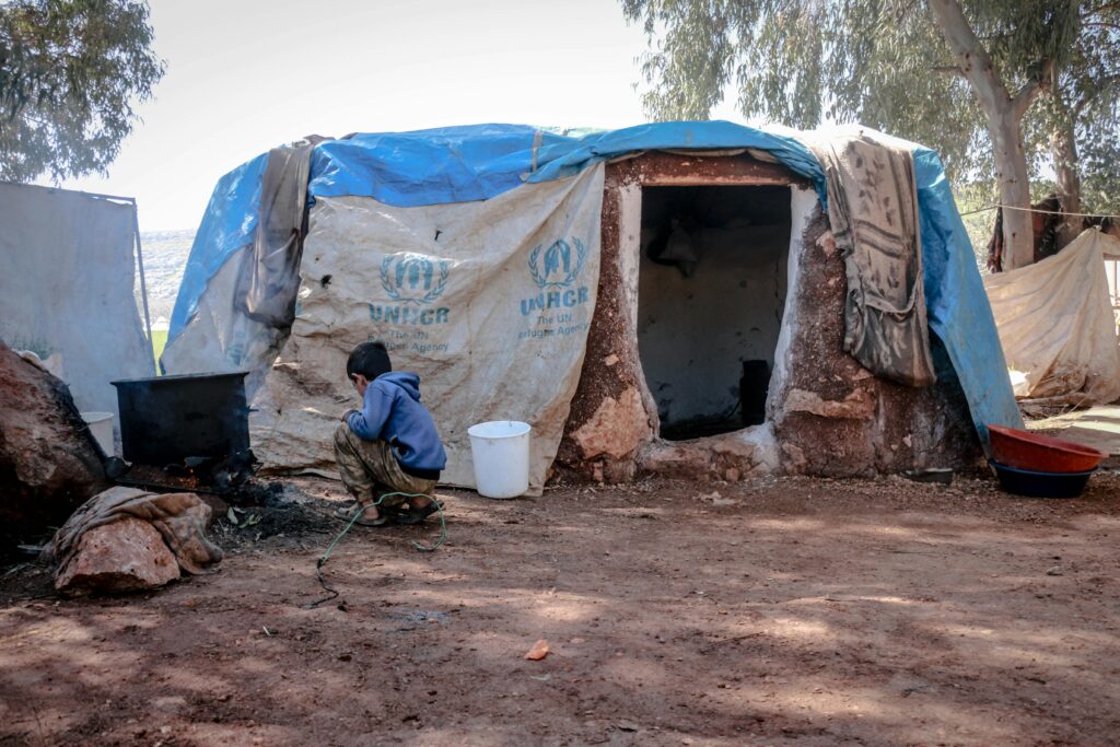 An outdoor scene showing a boy near a makeshift shelter in Idlib, highlighting living conditions.