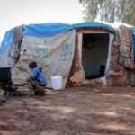 Right to Housing Upheld: High Court Orders Fresh Review of Flats Allocation for Jhuggi Dwellers An outdoor scene showing a boy near a makeshift shelter in Idlib, highlighting living conditions.