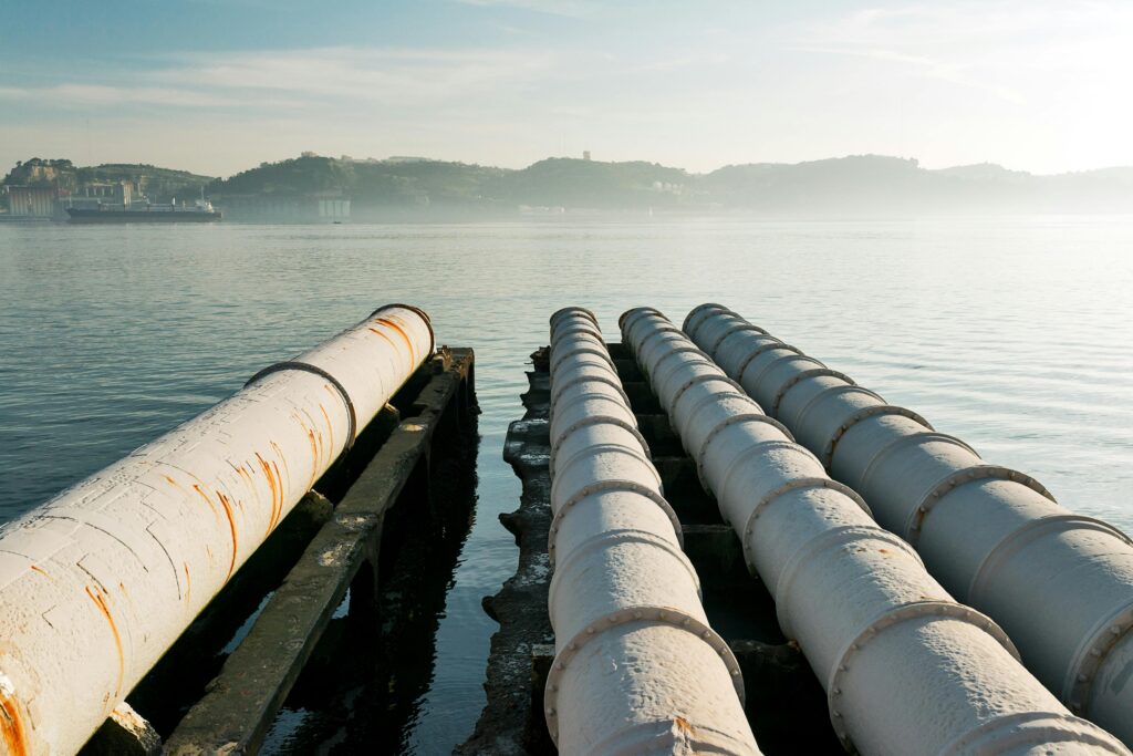 Sewage pipes stretch over a tranquil waterfront in Lisbon, highlighting urban infrastructure.
