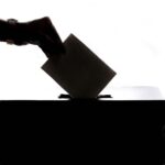 Silhouette of a hand placing a vote into a ballot box, symbolizing democracy.