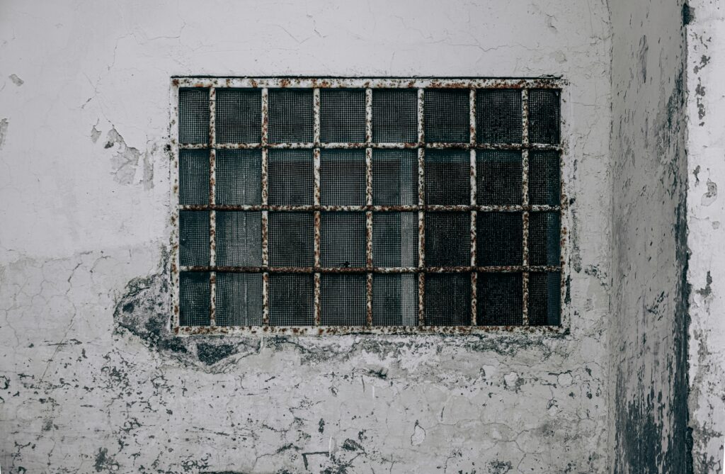 A weathered wall with a rusty barred window, showcasing decay and urban texture.