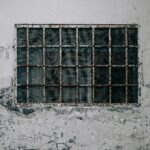 A weathered wall with a rusty barred window, showcasing decay and urban texture.