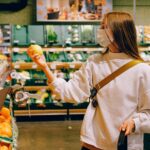 A woman wearing a face mask shops for fruit in a supermarket, focusing on healthy choices.