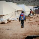 A young boy carrying a backpack walks in a refugee camp in Idlib, Syria.