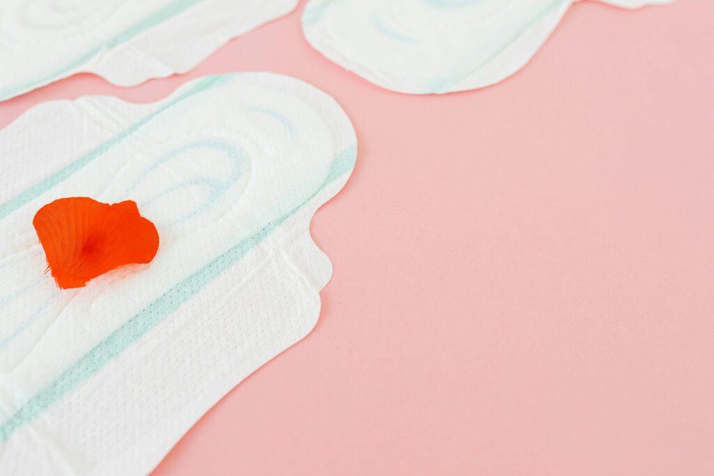Close-up of sanitary pads with a red rose petal on a pink background, symbolizing menstruation.