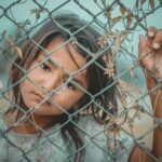 A thoughtful child gazes through a wire fence, symbolizing innocence and curiosity.