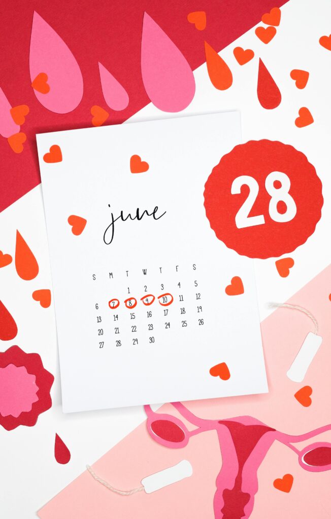 Artistic still life of a June calendar with heart and blood drop cutouts symbolizing the menstrual cycle.