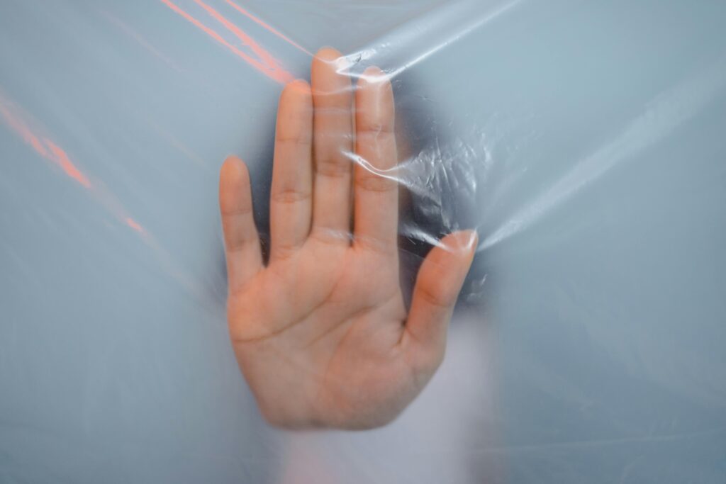A close-up of a hand pushing against a translucent plastic sheet, suggesting themes of confinement or barrier.