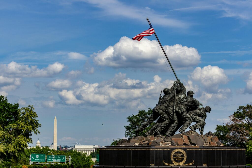 Iwo Jima Memorial with American flag and Washington Monument under blue skies.