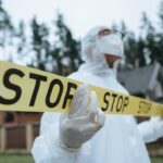Investigator in protective gear securing crime scene with stop tape outdoors.