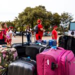 Group of travelers with colorful luggage at outdoor parking area.