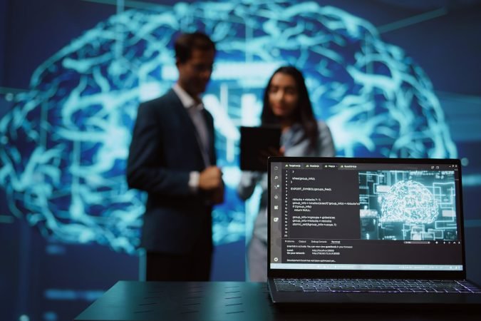 Focus on laptop in workspace used by AI researchers working with artificial intelligence in blurry background. Close up of notebook used by employees developing AI systems in tech startup, camera B
