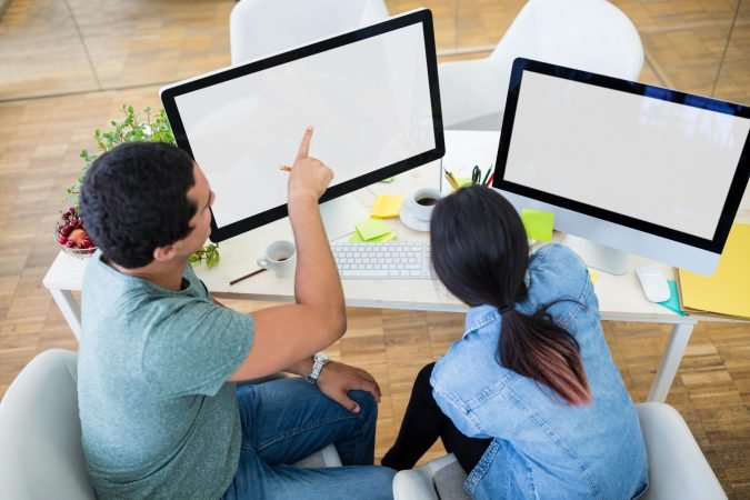 Male and female graphic designers interacting over computer in office